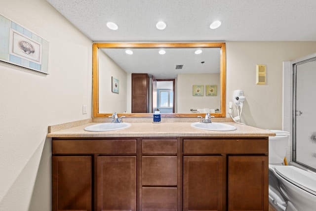 bathroom with a textured ceiling, dual bowl vanity, and toilet