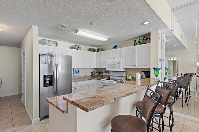 kitchen with a kitchen breakfast bar, white appliances, a peninsula, white cabinets, and light stone countertops