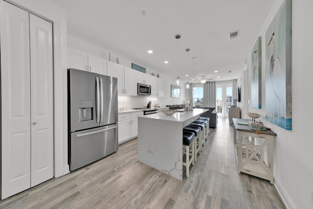 kitchen featuring pendant lighting, appliances with stainless steel finishes, light hardwood / wood-style flooring, and a center island with sink