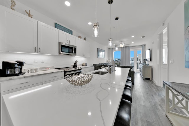 kitchen featuring decorative light fixtures, stainless steel appliances, light hardwood / wood-style floors, white cabinetry, and sink