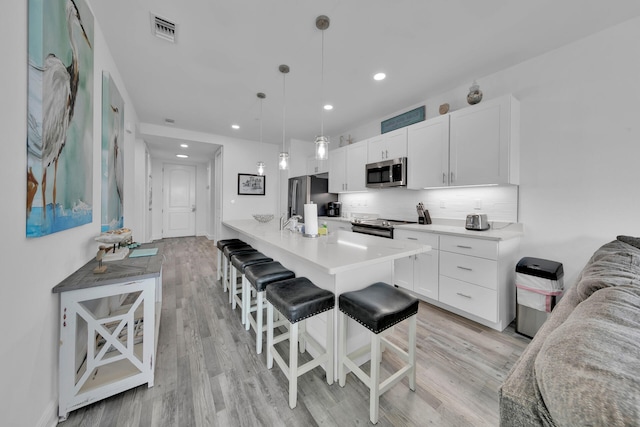 kitchen with pendant lighting, white cabinets, a breakfast bar, light wood-type flooring, and appliances with stainless steel finishes