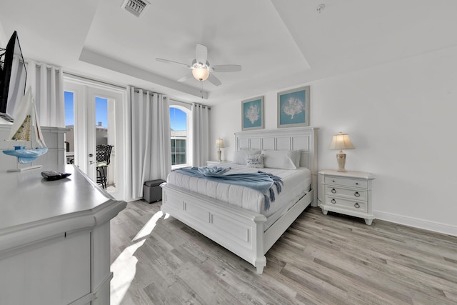 bedroom with ceiling fan, a tray ceiling, and light wood-type flooring