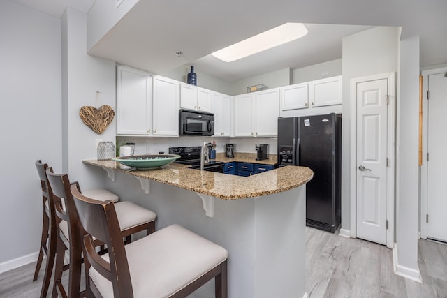 kitchen with black appliances, white cabinets, kitchen peninsula, and dark stone countertops