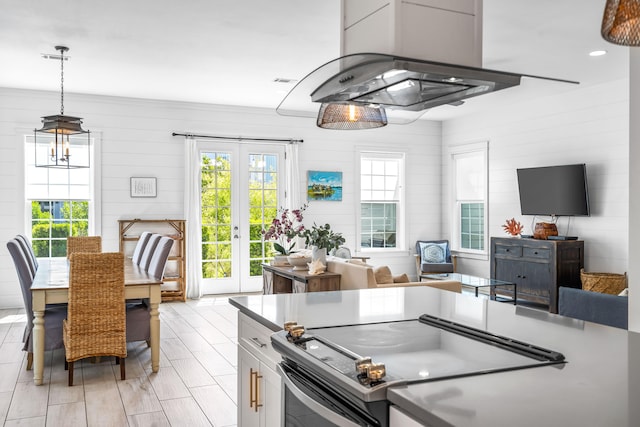 kitchen with white cabinetry, decorative light fixtures, stainless steel range with electric stovetop, island exhaust hood, and french doors