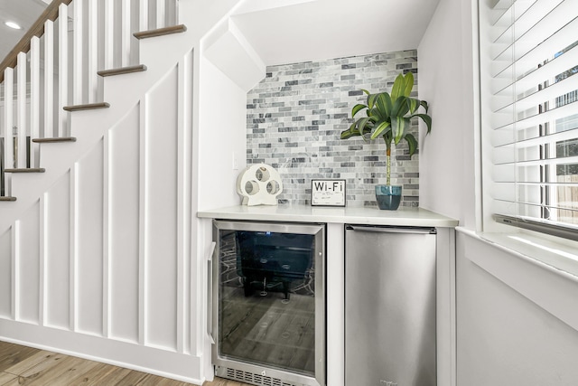 bar featuring refrigerator, wine cooler, light hardwood / wood-style floors, and tasteful backsplash