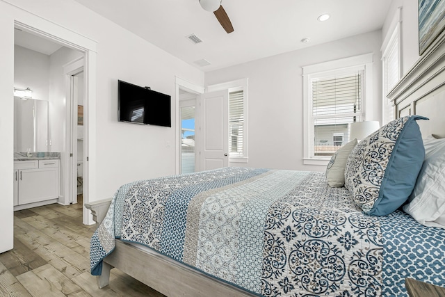 bedroom with ensuite bathroom, ceiling fan, sink, and light wood-type flooring