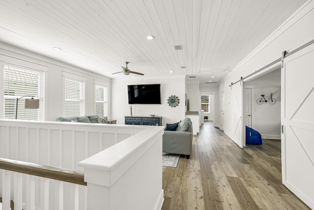 living room with a wealth of natural light, ceiling fan, light hardwood / wood-style floors, and a barn door