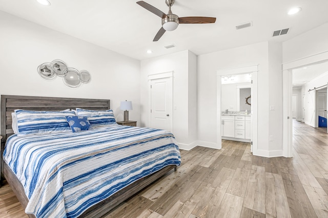 bedroom featuring a barn door, ensuite bath, ceiling fan, light hardwood / wood-style floors, and a closet