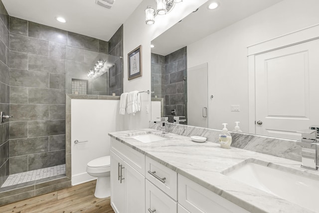 bathroom featuring hardwood / wood-style flooring, toilet, double vanity, and a tile shower