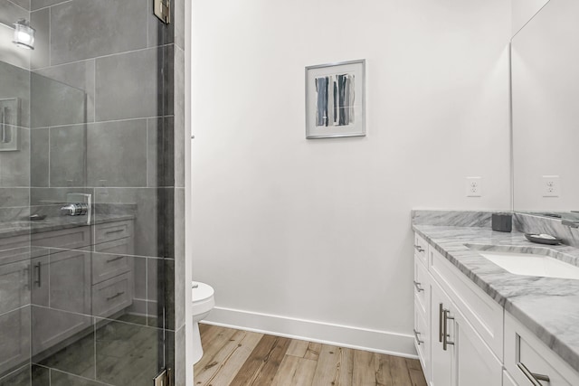 bathroom with a shower with door, wood-type flooring, vanity with extensive cabinet space, and toilet