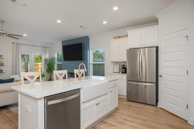 kitchen featuring white cabinetry, stainless steel appliances, crown molding, light hardwood / wood-style floors, and a center island with sink