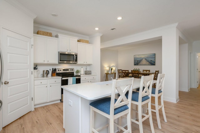 kitchen with white cabinets, a kitchen island with sink, appliances with stainless steel finishes, and light hardwood / wood-style flooring