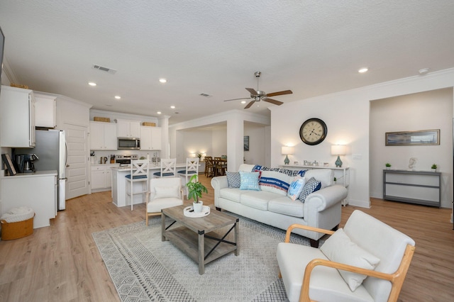 living room with ceiling fan, ornamental molding, a textured ceiling, and light wood-type flooring