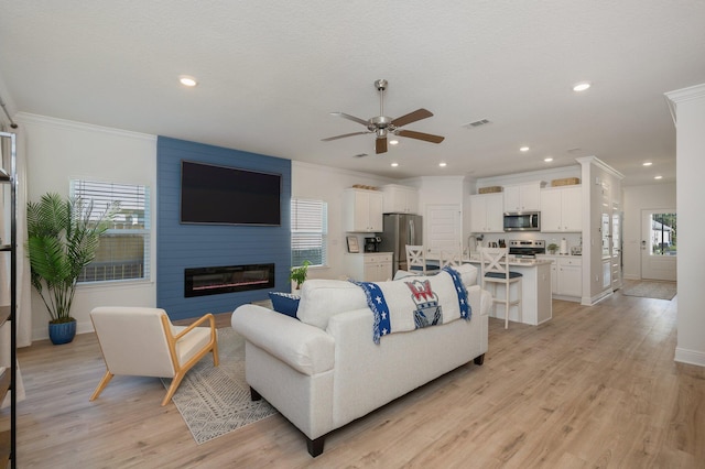 living room featuring a large fireplace, ceiling fan, light hardwood / wood-style flooring, and ornamental molding