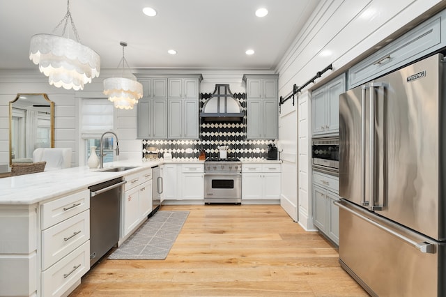 kitchen featuring a barn door, decorative light fixtures, light hardwood / wood-style flooring, custom exhaust hood, and high quality appliances