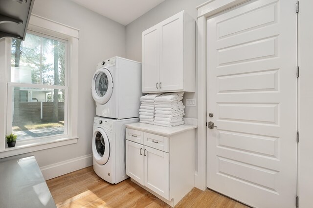 clothes washing area with light hardwood / wood-style floors, stacked washer / dryer, and cabinets