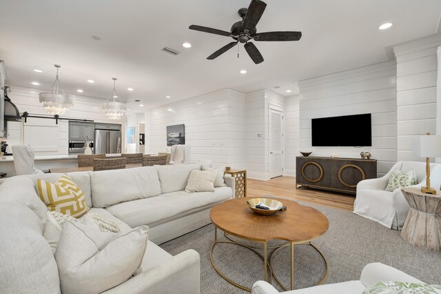 living room with ceiling fan with notable chandelier and light hardwood / wood-style floors