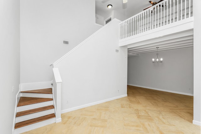 staircase featuring a towering ceiling, light tile floors, and an inviting chandelier