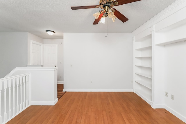 spare room featuring built in shelves, light hardwood / wood-style floors, ceiling fan, and a textured ceiling