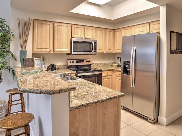 kitchen with light brown cabinets, light stone countertops, appliances with stainless steel finishes, a kitchen breakfast bar, and light tile floors