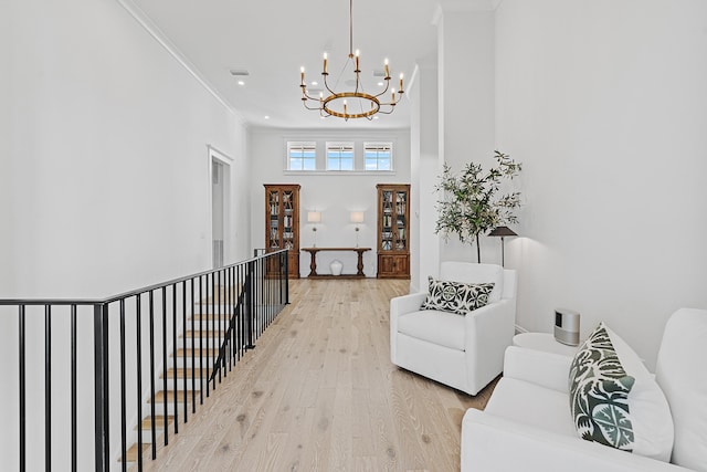 hallway with a notable chandelier, light hardwood / wood-style floors, crown molding, and a high ceiling