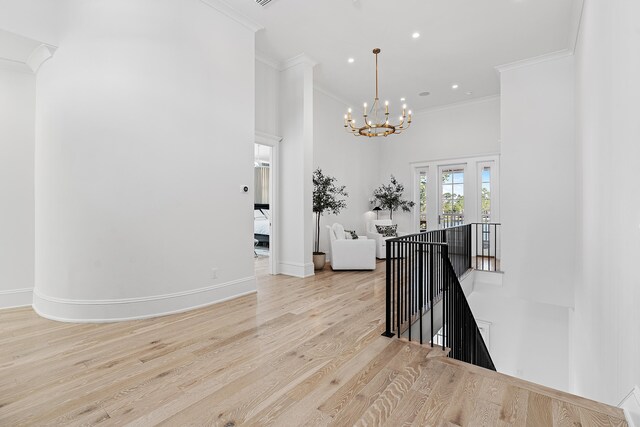 hallway with a high ceiling, light hardwood / wood-style floors, an inviting chandelier, and crown molding