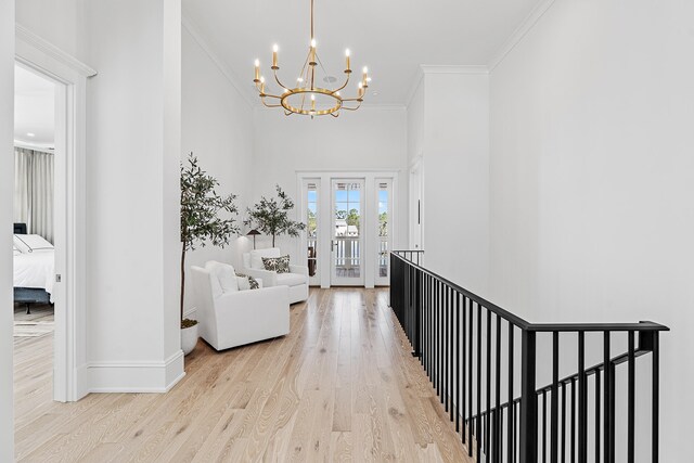 hall featuring an inviting chandelier, crown molding, light hardwood / wood-style flooring, and a towering ceiling