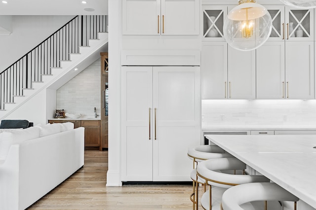 kitchen featuring decorative light fixtures, light hardwood / wood-style floors, backsplash, and white cabinetry