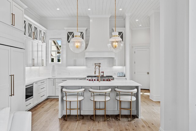 kitchen featuring white cabinets, light wood-type flooring, custom range hood, and a breakfast bar area