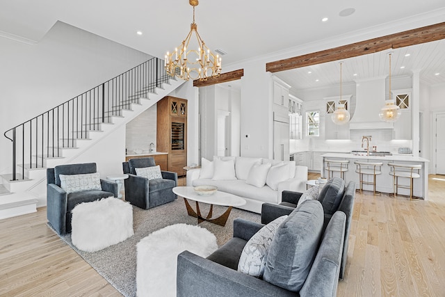 living room featuring beamed ceiling, sink, light hardwood / wood-style floors, crown molding, and an inviting chandelier