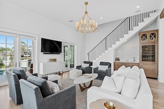 living room featuring french doors, ornamental molding, light hardwood / wood-style floors, and a notable chandelier