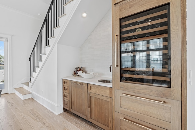 bar featuring crown molding, light hardwood / wood-style floors, and sink