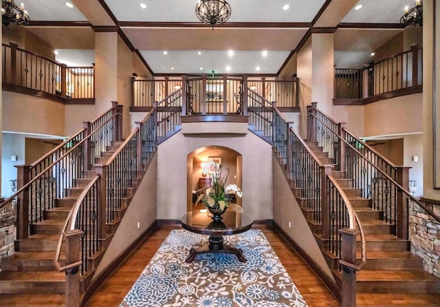 stairway featuring a high ceiling, wood-type flooring, crown molding, and a chandelier