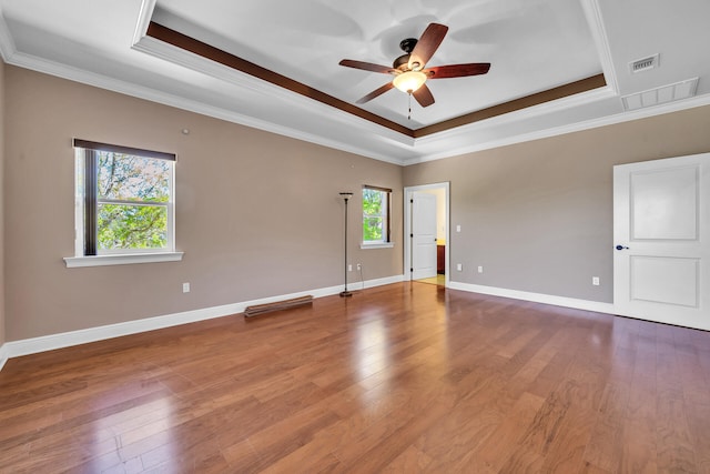 empty room with a tray ceiling, ceiling fan, crown molding, and hardwood / wood-style flooring