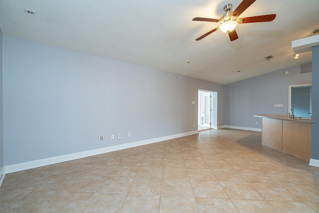 unfurnished living room featuring lofted ceiling, ceiling fan, light tile floors, and a textured ceiling