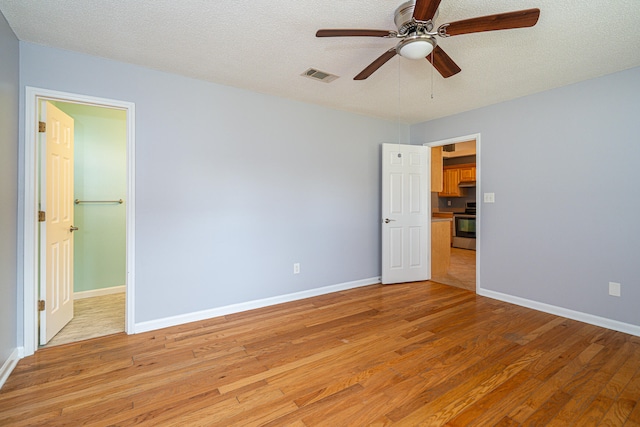 unfurnished bedroom with light hardwood / wood-style flooring, ceiling fan, a walk in closet, and a textured ceiling