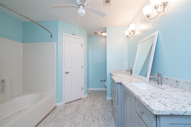 full bathroom with tiled shower / bath combo, oversized vanity, dual sinks, ceiling fan, and a textured ceiling