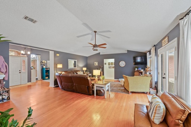 living room featuring ceiling fan with notable chandelier, vaulted ceiling, a textured ceiling, and light wood-type flooring