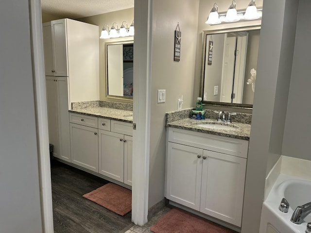 bathroom with vanity, wood-type flooring, a textured ceiling, and a tub to relax in