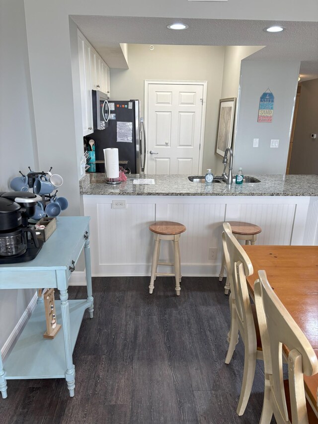 kitchen with white cabinets, light stone countertops, kitchen peninsula, and sink