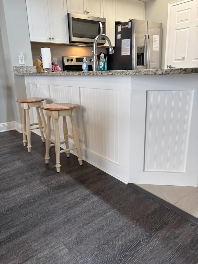 kitchen featuring white cabinetry, light stone countertops, stainless steel appliances, dark hardwood / wood-style flooring, and a kitchen bar