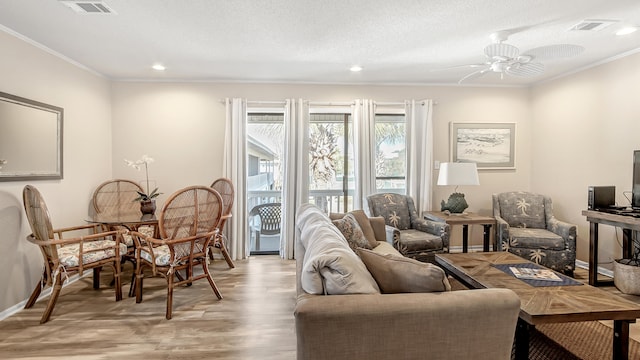 living room featuring ornamental molding, light hardwood / wood-style flooring, ceiling fan, and a textured ceiling