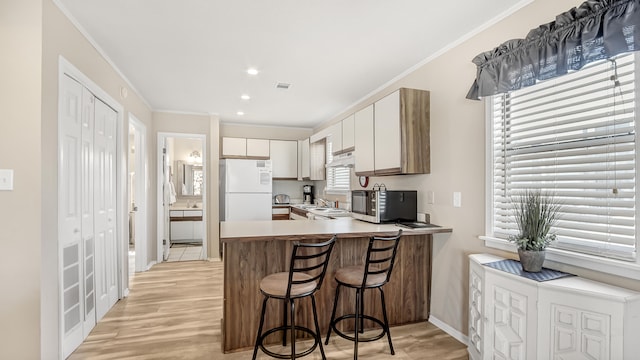 kitchen with light hardwood / wood-style floors, kitchen peninsula, white fridge, and crown molding