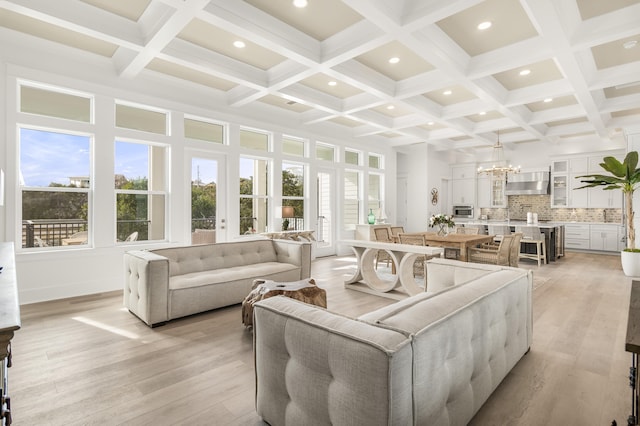 living room with an inviting chandelier, light hardwood / wood-style flooring, and beamed ceiling