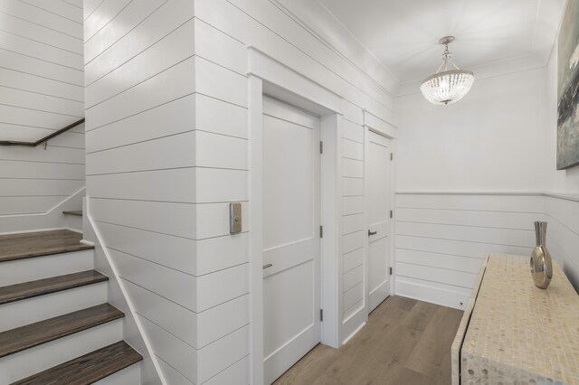 interior space featuring wooden walls, ornamental molding, a chandelier, and light wood-type flooring