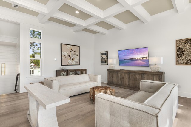 living room with coffered ceiling, beam ceiling, a high ceiling, and light wood-type flooring