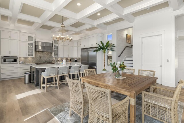 dining space with beamed ceiling, coffered ceiling, an inviting chandelier, and light wood-type flooring