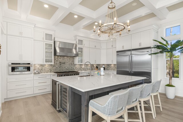 kitchen featuring white cabinetry, stainless steel appliances, a kitchen island with sink, and wall chimney range hood