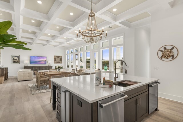 kitchen featuring sink, a center island with sink, light wood-type flooring, stainless steel dishwasher, and light stone countertops