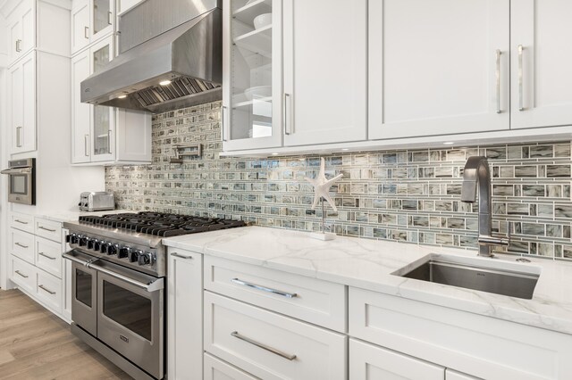 kitchen featuring white cabinetry, sink, stainless steel appliances, light stone countertops, and wall chimney range hood